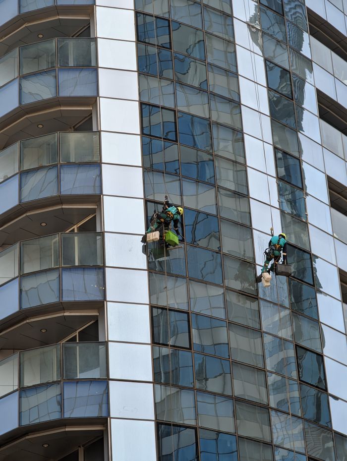 Des laveurs de vitres professionnels à l’œuvre sur un gratte-ciel à Abu Dhabi, mettant en valeur l’architecture urbaine.